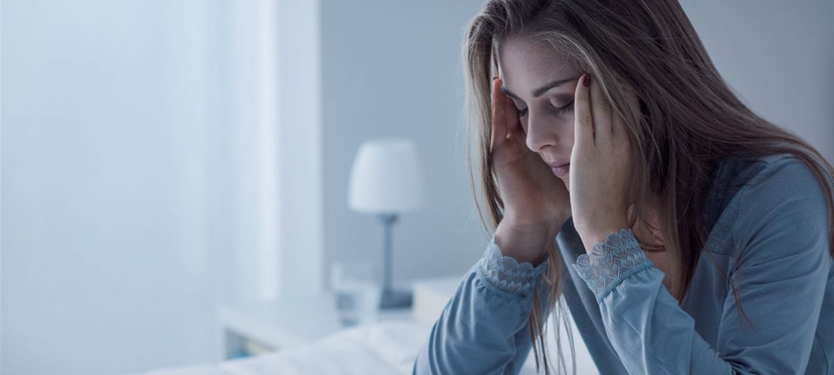 vrouw zit op bed met haar hoofd in haar handen