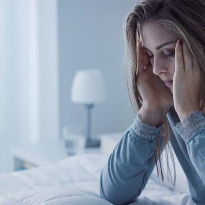 vrouw zit op bed met haar hoofd in haar handen