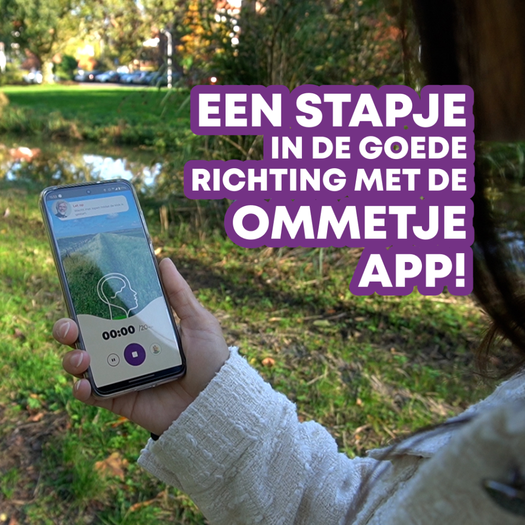 Een persoon houdt een smartphone vast met daarop de Ommetje-app geopend, terwijl diegene buiten op een wandelpad staat. Rechts in beeld staat de tekst: "Een stapje in de goede richting met de Ommetje app!" in paarse letters.